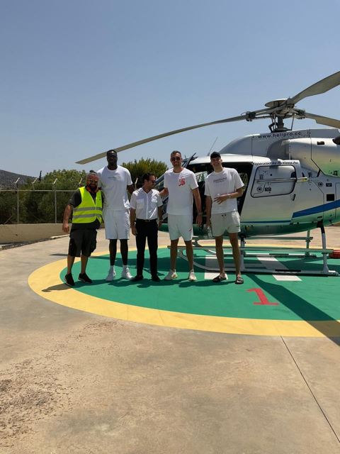 VIP passengers and crew posing on a helipad in front of a private helicopter for a charter transfer to Schinoussa, Greece