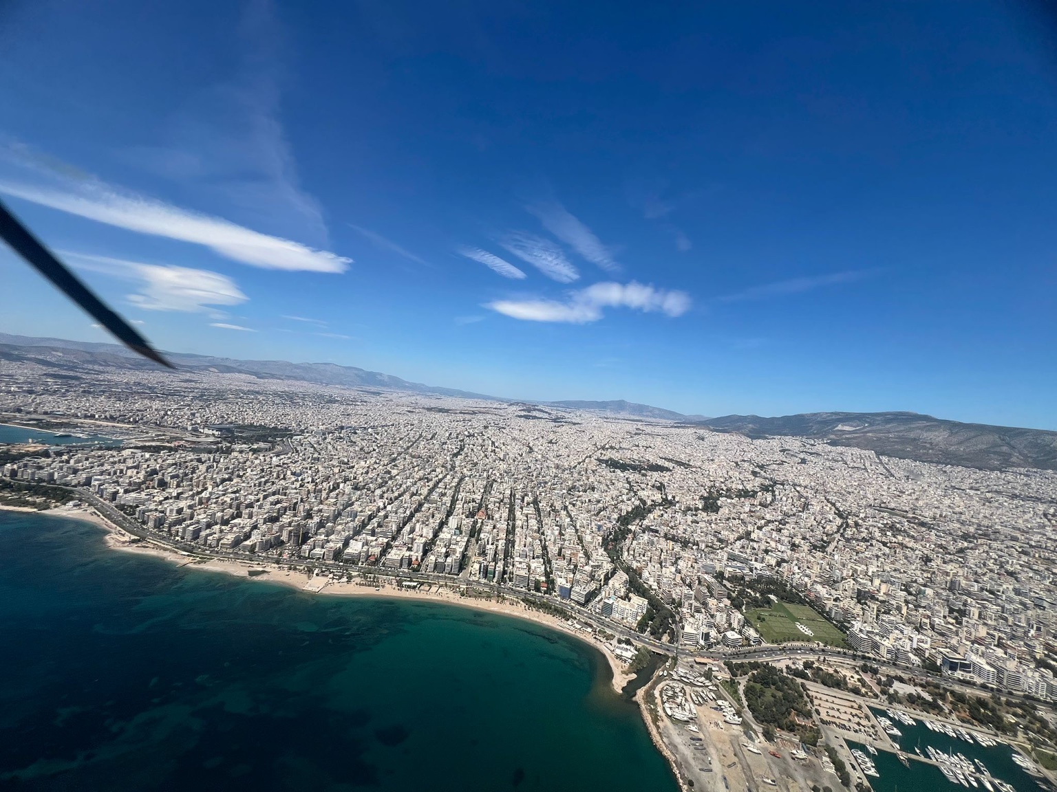 Approaching Athens from Antiparos aboard a Fly G Aviation Airbus H135, with the Athens Riviera and coastal skyline visible below.