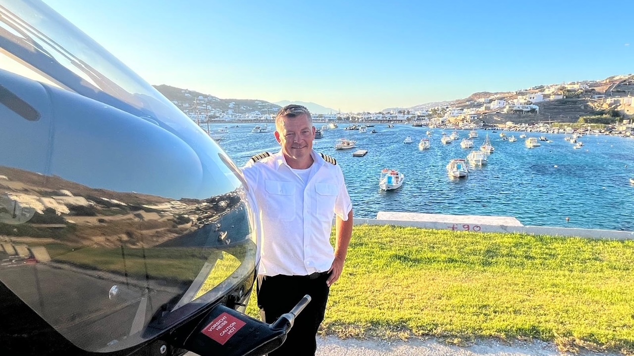 Franz Steier helicopter pilot with 5600 flight hours and EASA CPL licence beside helicopter overlooking coastal Greece
