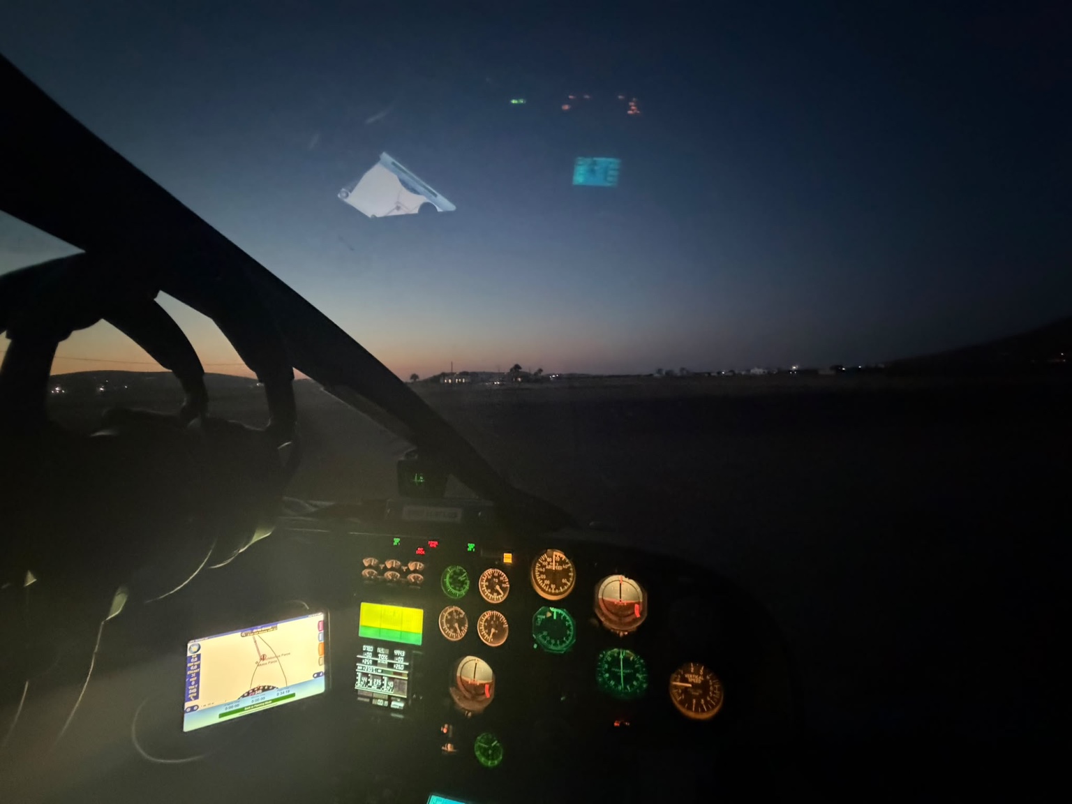 Cockpit view during final helicopter approach to a private helipad in Mykonos at sunset, moments before landing during the last VFR light.